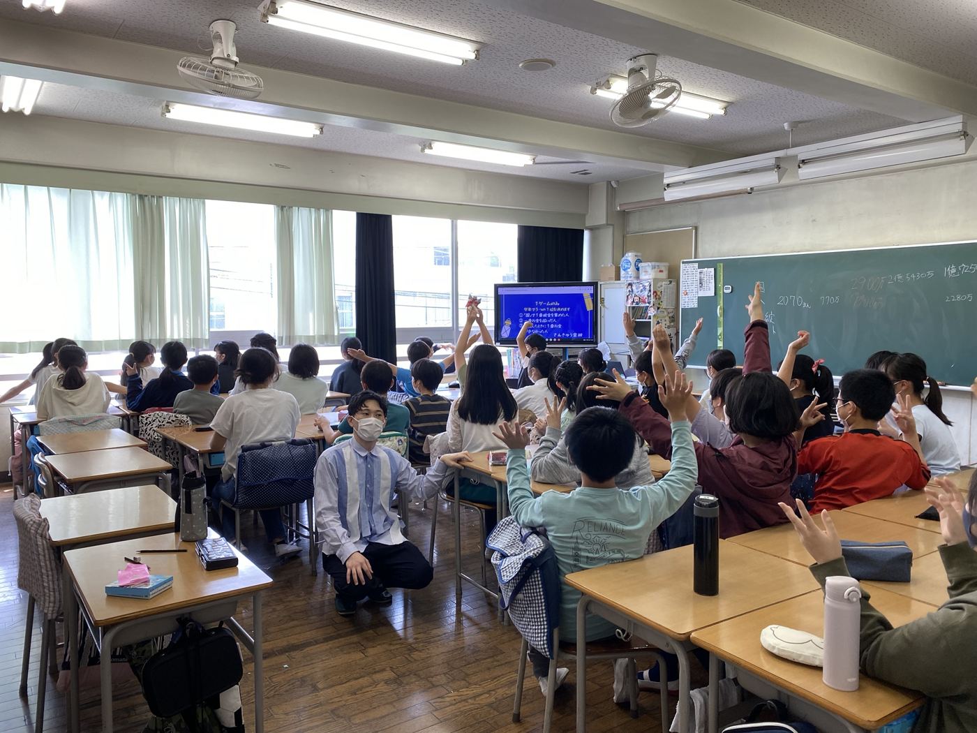 小学校の教室で、手を挙げて授業に参加する子どもたち